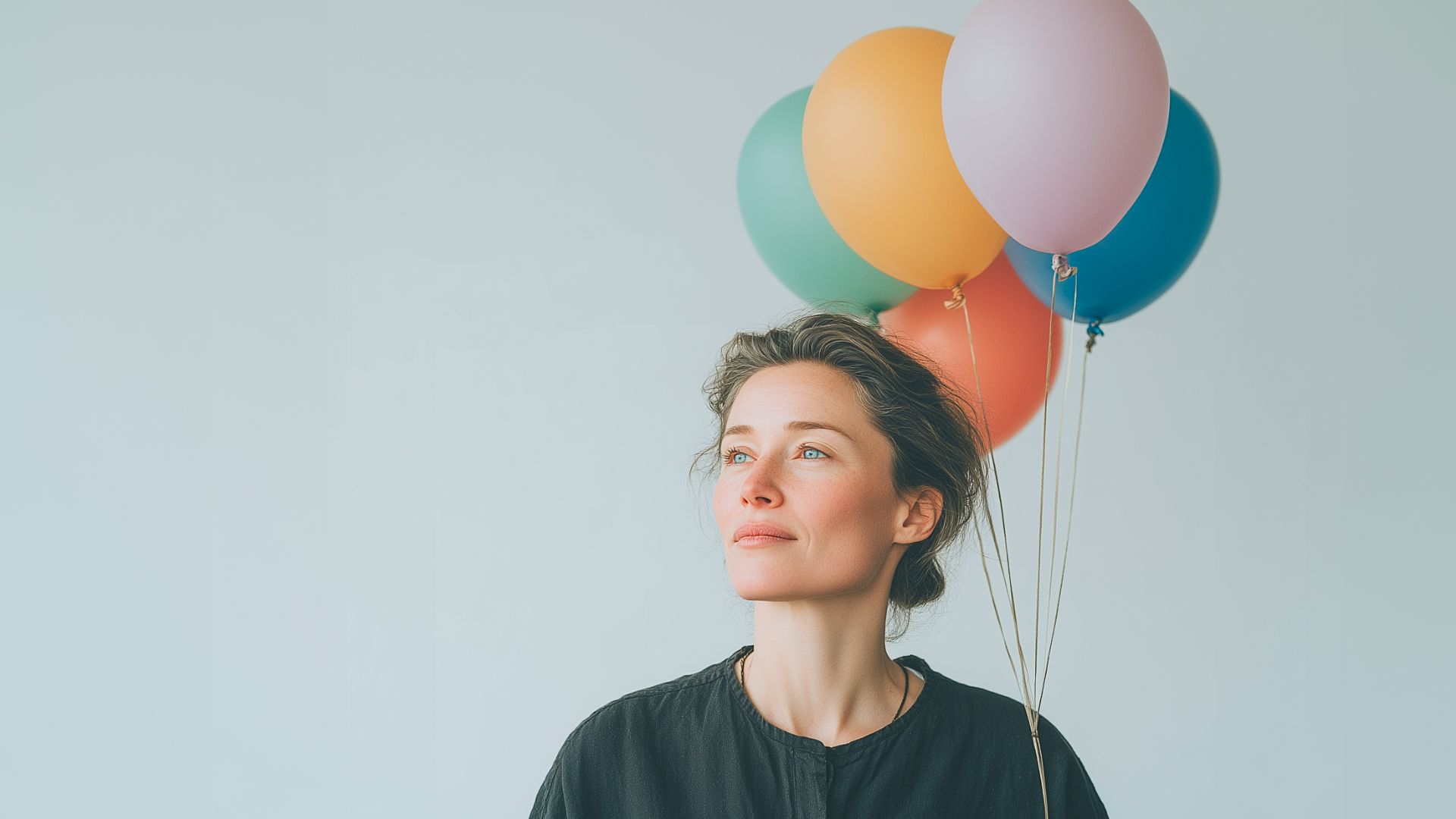 Kvinna med lugnt uttryck står mot ljus bakgrund och håller färgglada ballonger i handen. Bilden förmedlar en känsla av hopp, framtidstro och kreativitet
